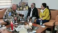 Ein Soldat und zwei Zivilisten sitzen an einem Tisch und besprechen etwas