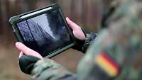 Ein Soldat im Gelände hält ein Tablet in der Hand.