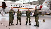 Vier Soldaten stehen in grüner Flecktarn-Uniform in einer Halle. Im Hintergrund steht ein weißes Flugzeug.