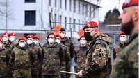 Ein Soldat im Tarnanzug spricht zu angetretenen Soldaten, die im Hintergrund erkennbar ist.