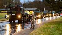 Mehrere LKWs stehen eng hintereinander in der Zufahrt einer Bundeswehr-Liegenschaft, ein Soldat weist die Fahrer ein.
