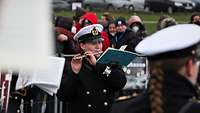 Mehrere Musiker in Marineuniform mit weißen Dienstmützen und mit Instrumenten.