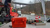 Ein roter Kasten mit vielen Kabeln steht unter einem Zeltdach auf einer abgesperrten Straße. 