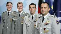 Vier Soldaten in grauen Uniformjacken mit Orden stehen vor Flaggen der NATO, EU und Deutschlands.