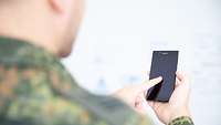 Blick über die Schulter: Ein Soldat tippt auf sein Smartphone.