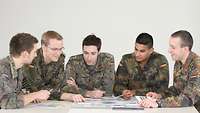 Fünf Soldaten sitzen gut gelaunt an einem Tisch und besprechen verschiedene Papiere und Bilder.