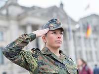 Eine Soldatin im Tarnanzug steht vor dem Bundestagsgebäude in Berlin und grüßt militärisch..