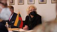 Ministerin Lambrecht sitzt mit weiteren Personen an einem Tisch, auf dem die Flagge von Litauen steht