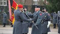 Ein Soldat übergibt eine schwarz-rot-goldene Fahne mit Bundesadler an einen zweiten. Dahinter stehen weitere Soldaten.