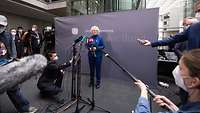 Ministerin Lambrecht steht vor einem Banner des Deutschen Bundestages und spricht in die Mikrofone der Pressevertreter.
