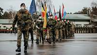 Soldaten marschieren mit Flaggen unterschiedlicher Nationen über einen Platz