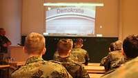 Soldaten sitzen in einem Unterrichtsraum und sehen einen Film auf einer Leinwand.