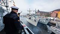 Zwei kleine graue Kriegsschiffe liegen in einem Hafen nebeneinander an einer Pier.