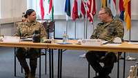 A female U.S. soldier and a German soldier sit next to each other at a table and talk