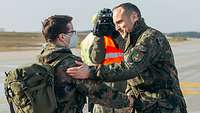 Auf einem Flughafen reicht ein Soldat einem anderen Soldaten mit Rucksack die Hand.