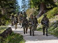 Eine Gruppe von Soldaten laufen mit Waffen einen Weg im Gebirge entlang.