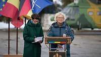 Ministerin Lambrecht steht an einem Rednerpult und spricht. Neben ihr steht eine Frau, die etwas aufschreibt.