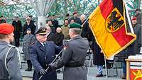 Ein Soldat übergibt an einen anderen eine Deutschlandflagge