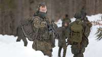 Mehrere Soldaten marschieren durch den verschneiten Wald. 