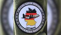 Ein rundes Patch, auf dem eine C-130J vor einem schwarz-rot-goldenen Deutschlandumriss zu sehen ist.