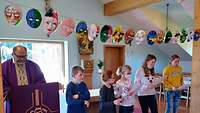 Kinder tragen die Fürbitten vor über ihnen hängen die selbst gebastelten Masken
