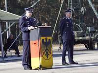 Zwei Soldaten stehen auf einem Platz. Einer steht hinter einem Pult und hält eine Rede. 