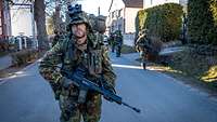 Ein bewaffneter Soldaten Nachtsichtgerät läuft vor Soldaten, die in Zweierreihe folgen.