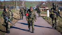 Auf einer Straße laufen Soldaten bergauf, vorn in der Mitte läuft einer mit einer roten Armbinde.