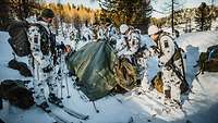 Mehrere Soldaten bereiten im verschneiten Gelände ein Zelt für den Transport eines Verunglückten vor. 