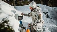 Ein Soldat hockt im Schnee vor einem Gaskocher und rührt in einem Topf.