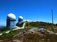 Zwei Gebäude mit einer runden Kuppel in der sich ein Radar verbirgt stehen auf einer Bergspitze.