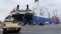 Ein Panzer fährt aus einem Schiff heraus, dass Schiff ist in voller Länge im Hintergrund zu sehen.