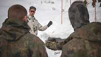 Zwei Soldaten stehen vor einem dritten Soldaten im Schneeanzug. Er erläutert ihnen etwas.