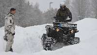 Ein Soldat fährt mit einem Quad im Schnee an einem Soldaten in Schneeanzug vorbei.