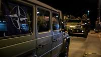 A military vehicle with a NATO symbol at the side window, another vehicle blurry in the background