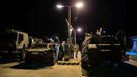 Two combat vehicles are refueled at a military filling station in the dark.