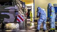 A soldier wearing protective gear sprays a combat vehicle with disinfectant solution.