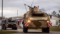 Several armored transport vehicles roll through a barracks gate