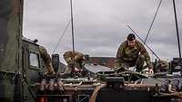 A soldier squats on the roof of a vehicle to check equipment.