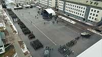 Many soldiers and tanks stand on a square surrounded by white buildings.