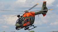 Ein Hubschrauber mit den Buchstaben SAR auf orangefarbenem Grund an der Seite hebt vom Flugfeld ab.