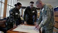 Two male and one female soldier look at a tactical map