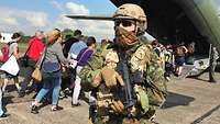 Zivilisten besteigen ein Flugzeug, davor steht ein Soldat mit seiner Waffe.