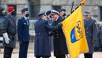 Ein Soldat übergibt einem anderen Soldaten eine Flagge. Im Hintergrund weitere Soldaten und die Burgmauer der Festung in Ulm.