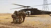 Zwei US-Soldaten und zwei deutsche Soldaten transportieren einen verwundeten Soldaten in einer Trage zu einem Hubschrauber