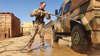 Ein Soldat steht mit einem Hochdruckreiniger an einem Gefechtsfahrzeug und reinigt die Räder 