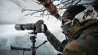 Ein Soldat im Schneetarn richtet eine Kamera aus.