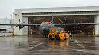 A C-130J, painted in the distinct air force gray with a German flag, is pulled out of a hangar.