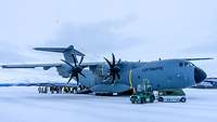 Ein Militärtransportflugzeug steht auf einer vereisten Landebahn und wird entladen.