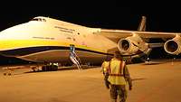 Ein Transportflugzeug Antonow AN-124 auf dem Flugplatz, davor zwei Soldaten